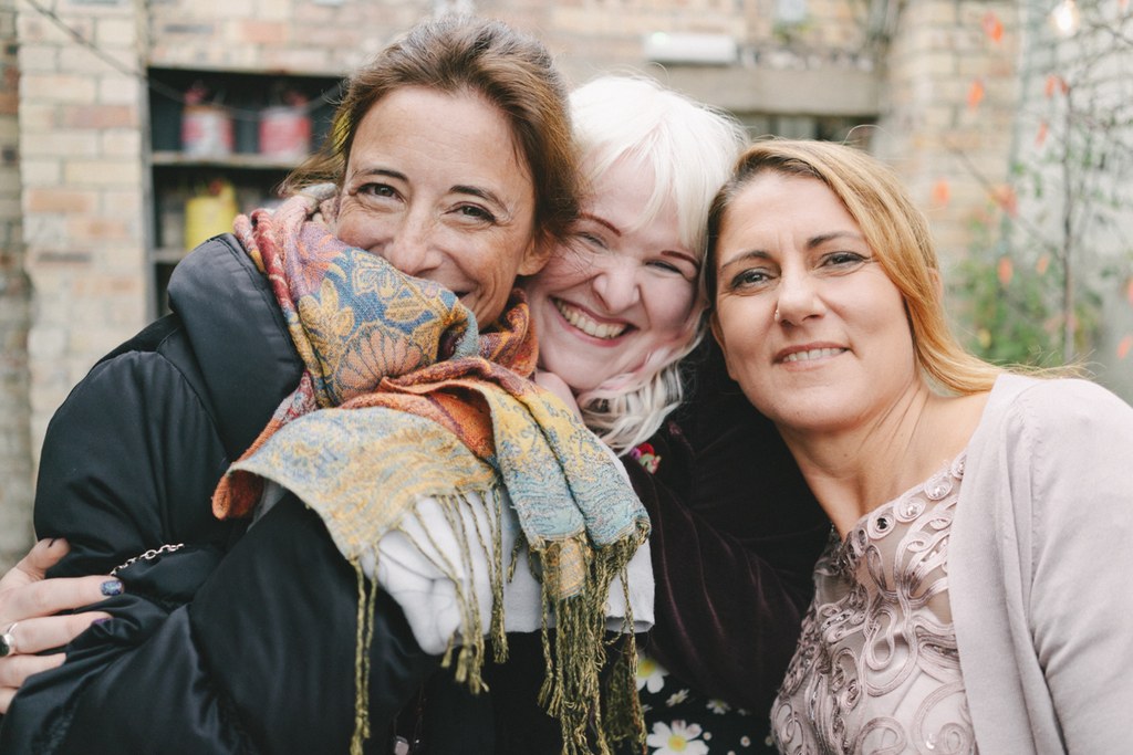 Three women in a close embrace laughing, a baby with a colourful scarf in the centre