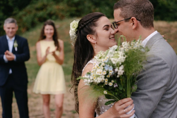 Smiling bride and groom at outdoor wedding with daisy bouquet, romantic garden ceremony moment.