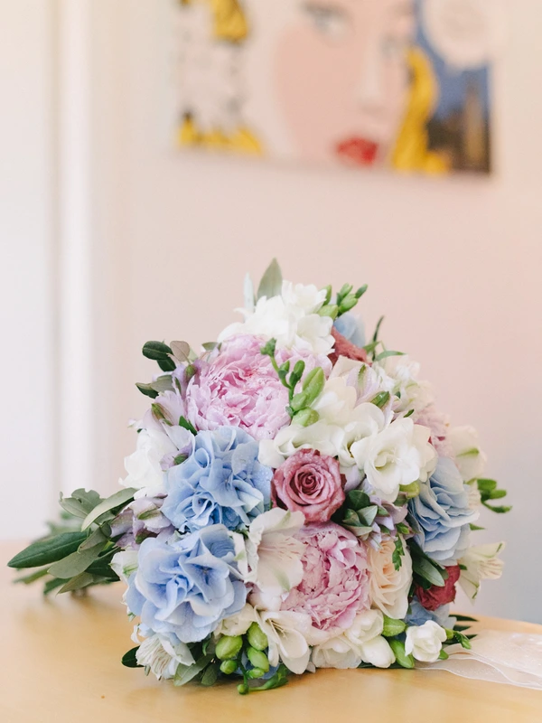 Romantic bridal bouquet on a light table — blue and pink peonies, white freesia and green leaves