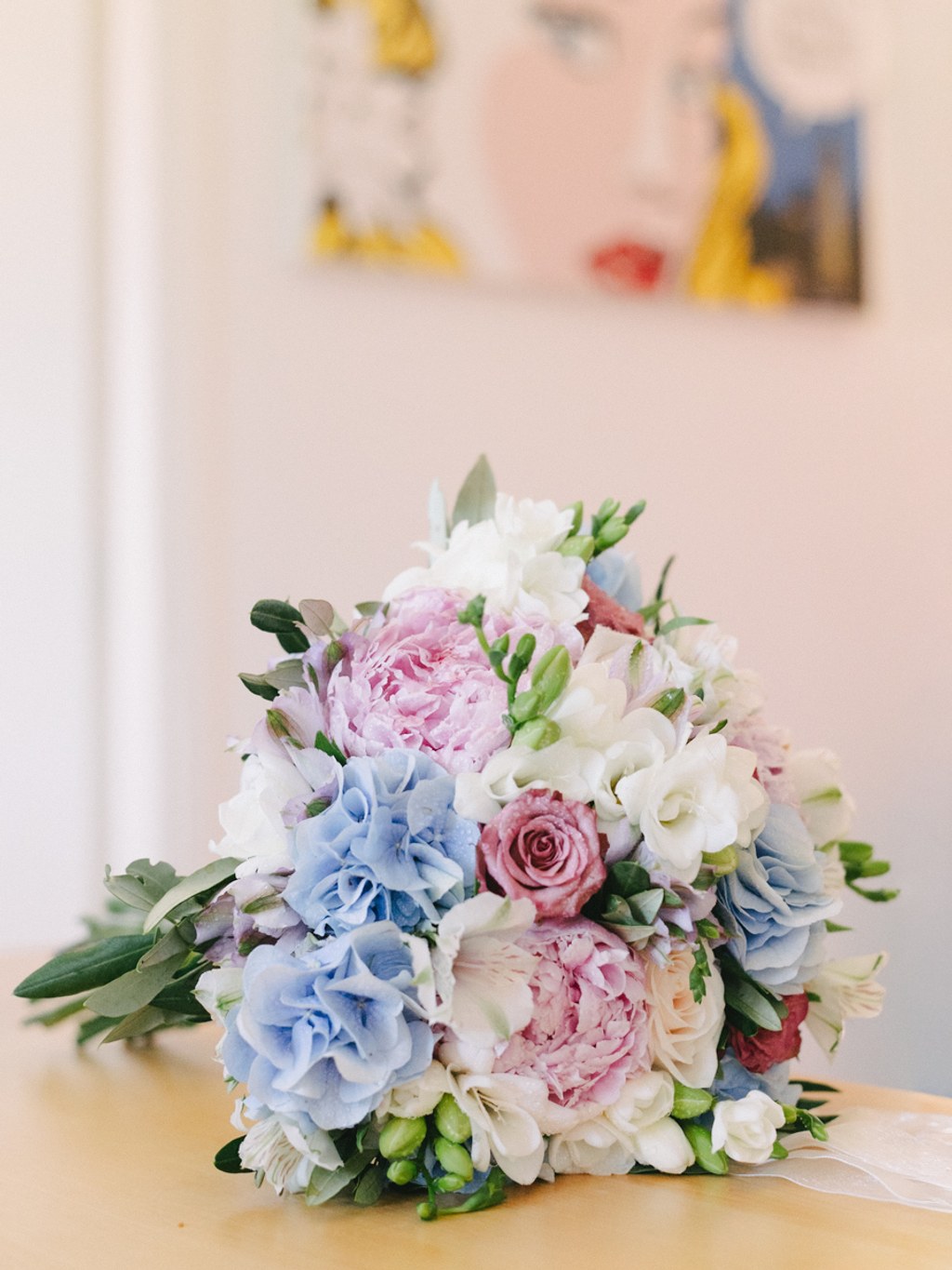 Romantic bridal bouquet on a light table — blue and pink peonies, white freesia and green leaves
