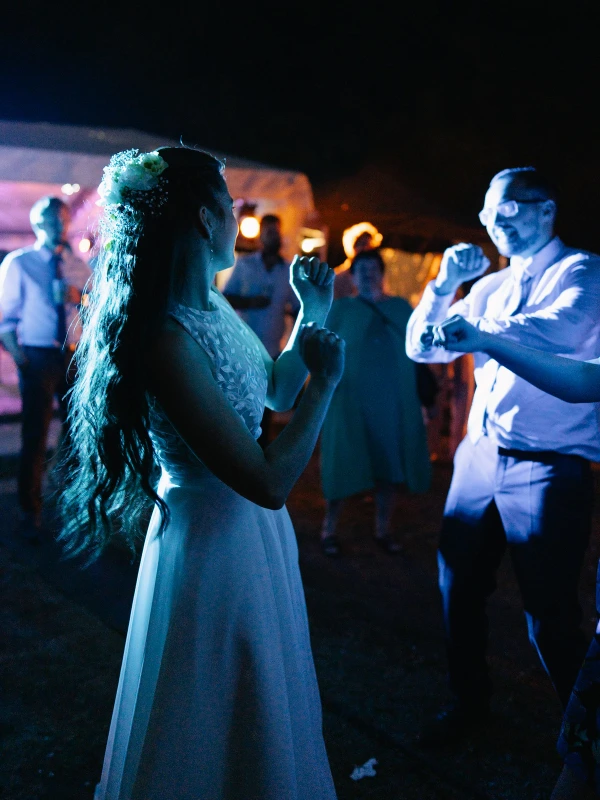 Bride dancing with guest at nighttime outdoor wedding celebration with blue ambient lighting.
