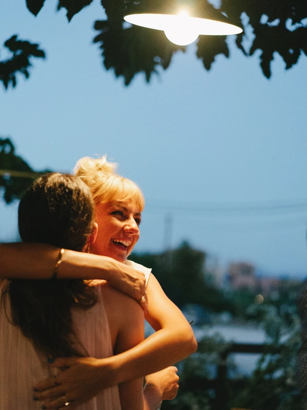 Smiling blonde woman hugs a man in a lovely evening moment — leafy branches, blue sky and city lights
