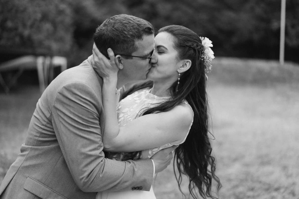 Black and white photo of groom kissing bride with tender expression during outdoor wedding ceremony.
