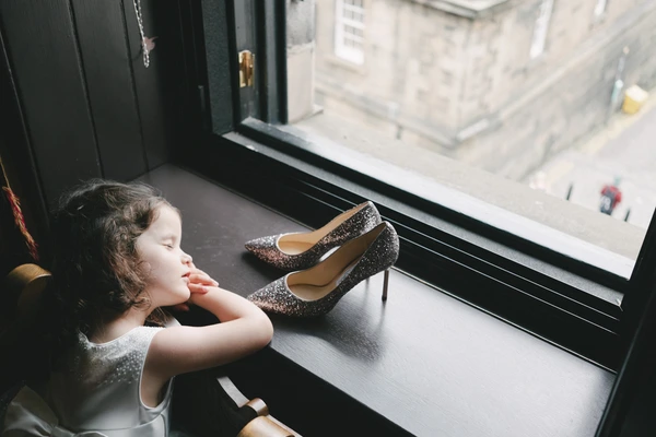 Little girl gazes at the elegant sparkling bridal shoes on the table with a thoughtful look