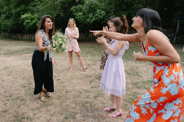 Bride and woman with bouquet laughing together during bouquet toss moment at outdoor wedding reception.