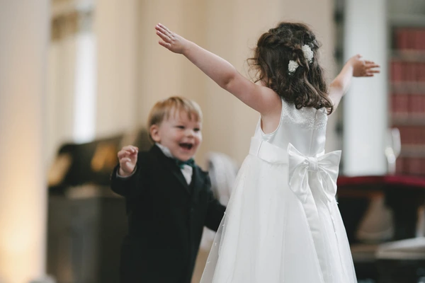 Little girl with white flower pin dances freely in the church, boy in black suit watching