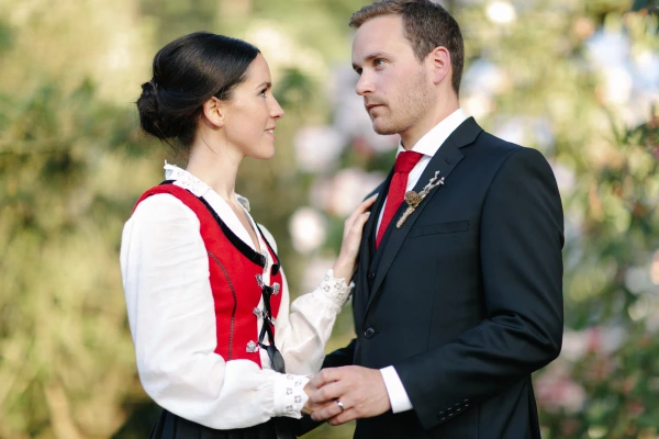 A close portrait of the bride in her Norwegian bunad looking up at the groom, who gazes back at her with a calm, intent expression. Candid documentary wedding portrait at the Royal Botanic Garden Edinburgh.