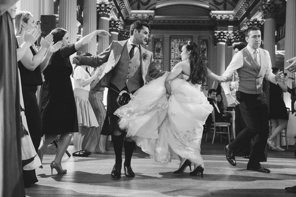 Bride and groom dance in the classical ballroom while guests applaud — bride's gown swirls