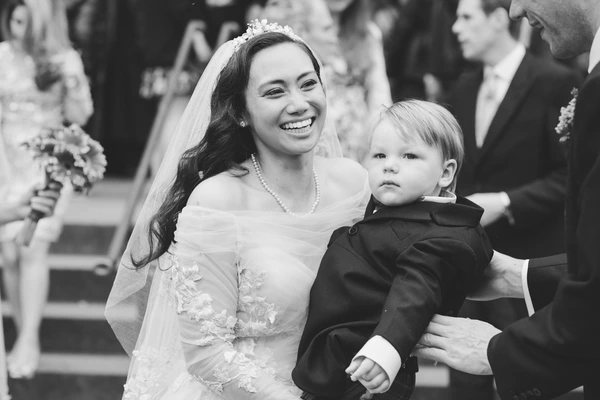 Bride in floral silk dress and veil with a radiant smile beside a little boy — black-and-white
