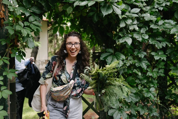 Happy guest or florist carrying a lush green fern bouquet through a garden gate.