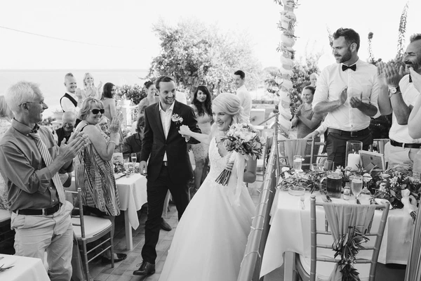 Bride and groom walk happily among guests at the terrace reception, floral decorations and tables