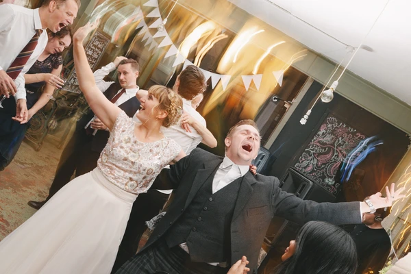 Bride and groom dance joyfully among guests in an elegant hall with golden and white decoration