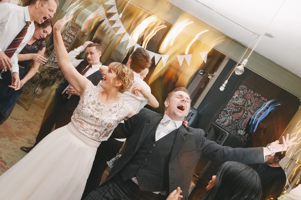 Bride and groom dance joyfully among guests in an elegant hall with golden and white decoration