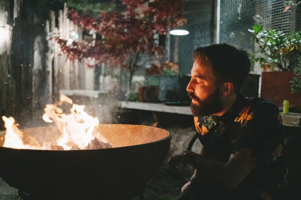 Bearded groom in dark suit sits by the fire on an autumn evening in the industrial courtyard