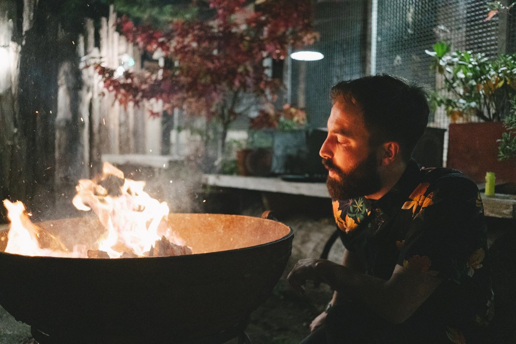Bearded groom in dark suit sits by the fire on an autumn evening in the industrial courtyard