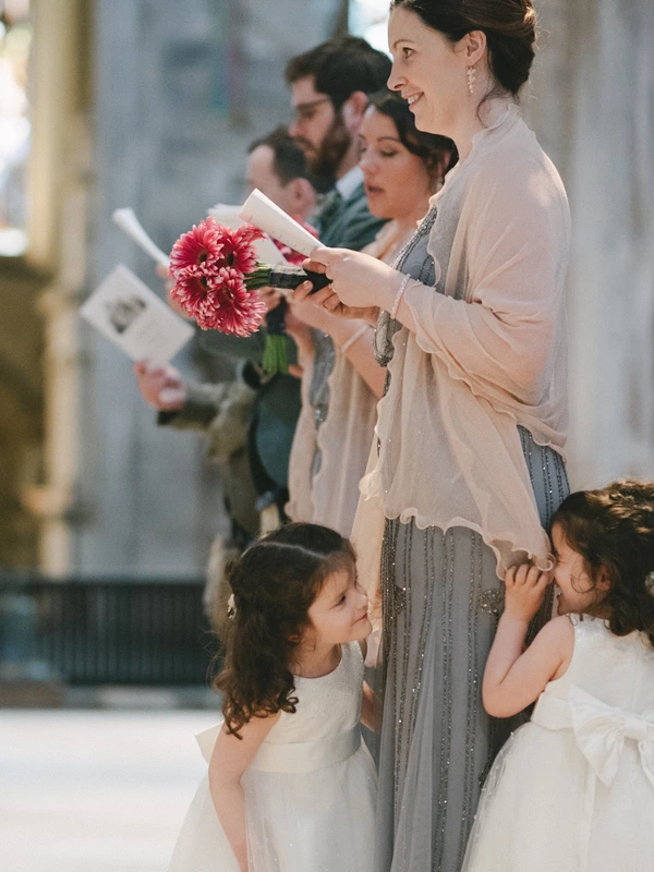 Woman in light dress holds pink bouquet at the ceremony, two little girls in white beside her