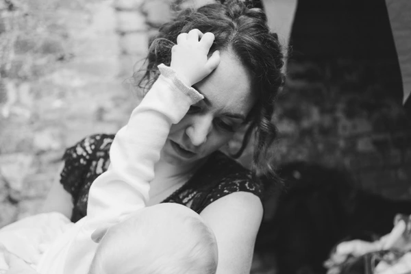 Mother in lace holds her infant lovingly against a stone wall — black-and-white portrait