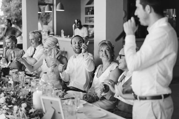 Wedding guests around the table laughing and chatting — bride and guests in white, flowers on the table