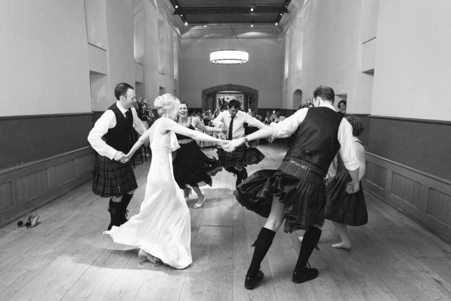 Black and white documentary picture of bride and groom ceilidh dancing in the Queen Ann room of the Edinburgh Castle