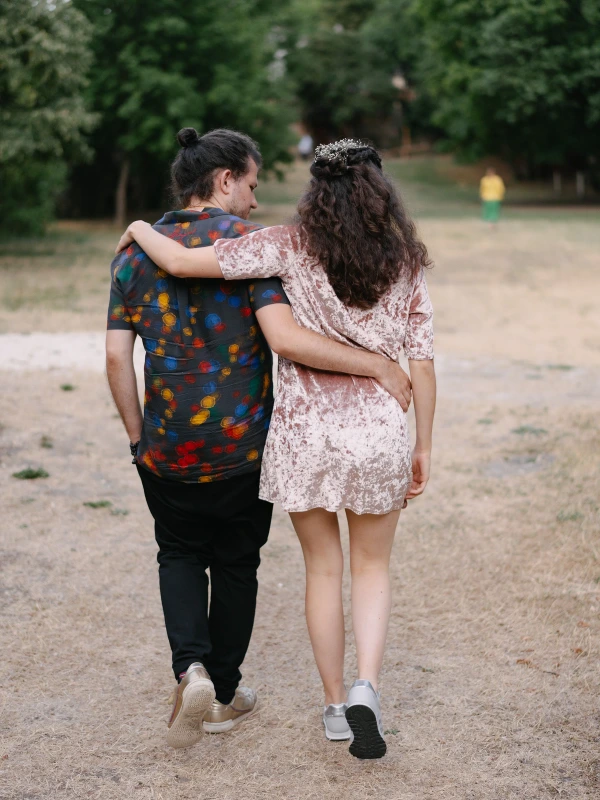 A couple walking together arm in arm at outdoor wedding with colorful patterned clothing in field.
