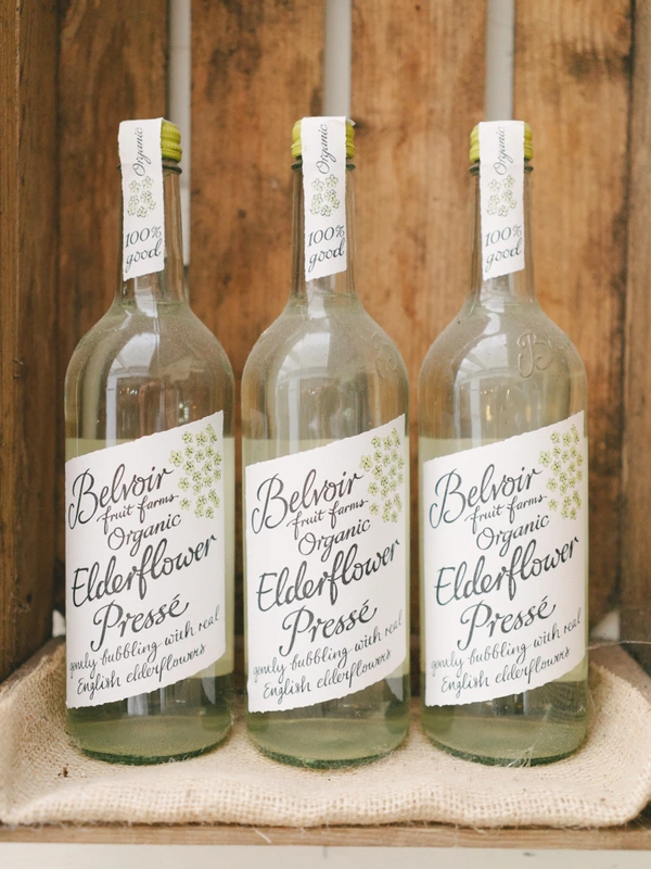 Three Belvoir elderflower sparkling drink bottles with white labels on canvas