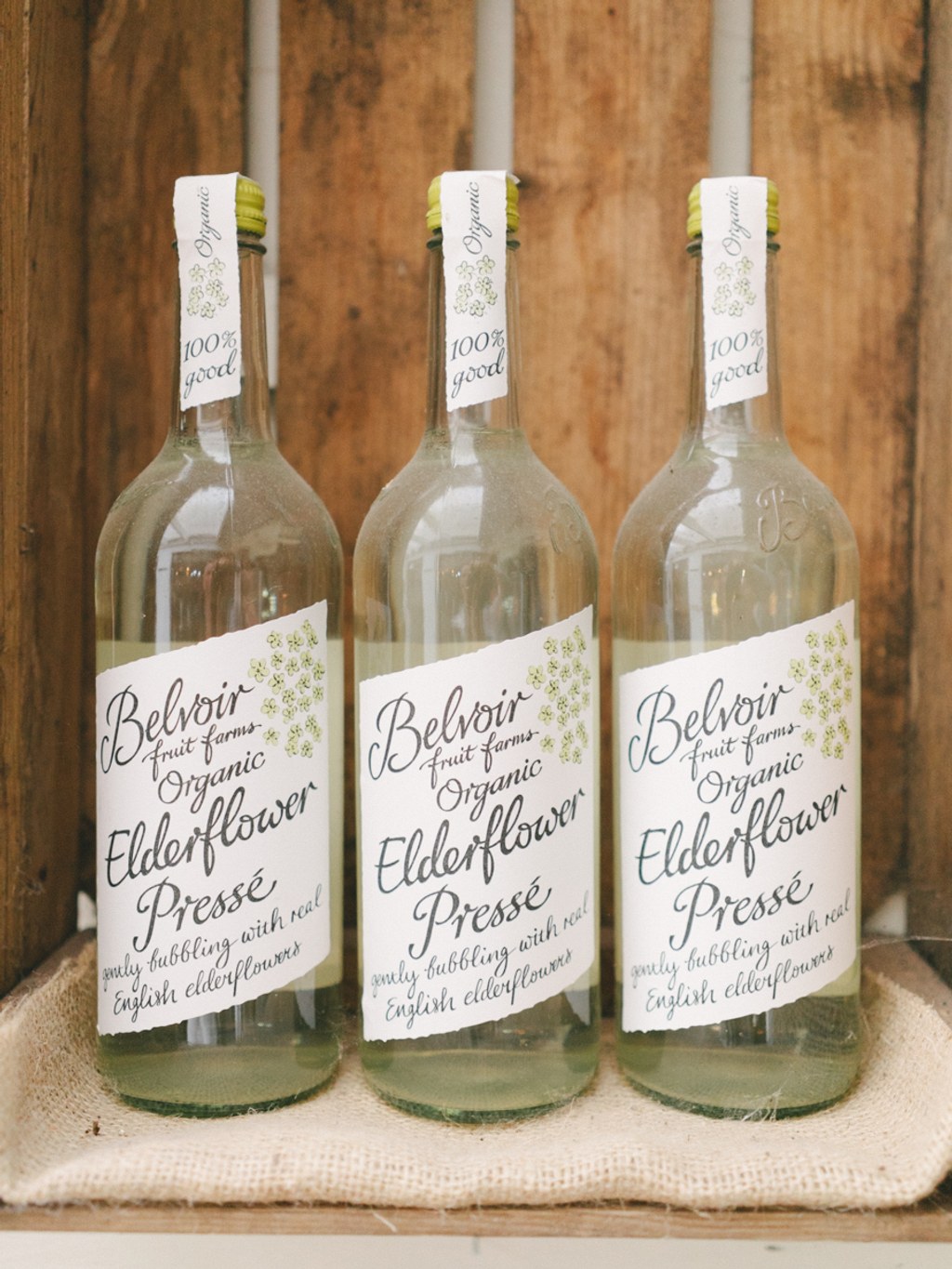 Three Belvoir elderflower sparkling drink bottles with white labels on canvas