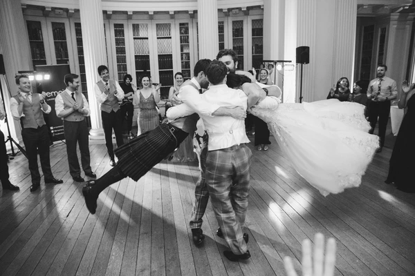 Bride and groom dance joyfully in the grand ballroom — groom in tartan kilt, bride's gown flowing