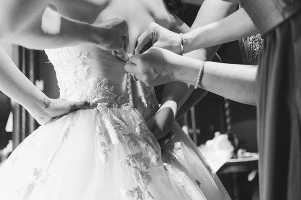 Multiple helping hands fasten the white lace gown — back buttons and jewel detail in focus