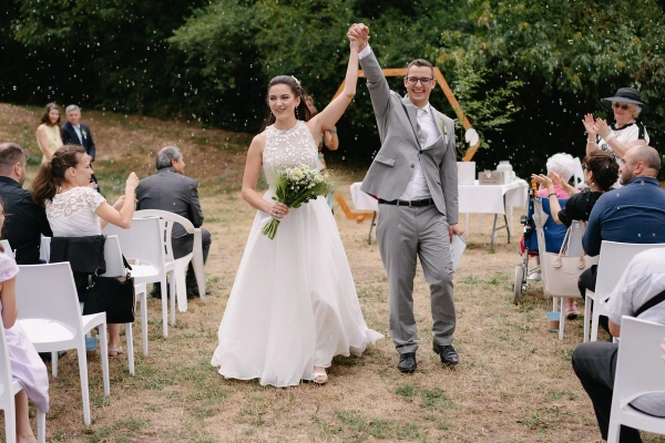 Newlyweds walking down aisle with hand raised in celebration under wooden hexagon arch at wedding.
