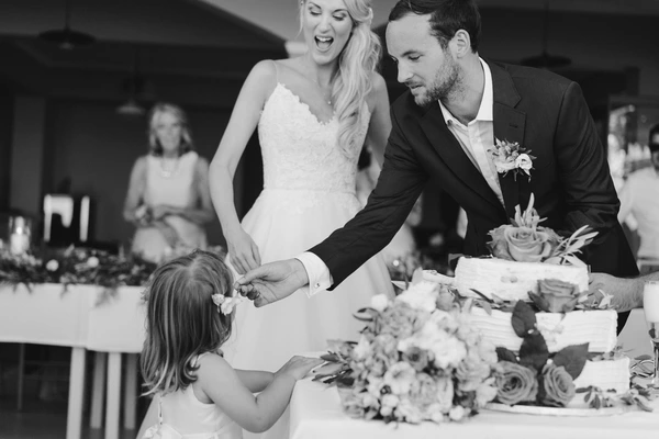 Groom puts a white flower in a little girl's hair at the dinner, joyful bride beside the cake