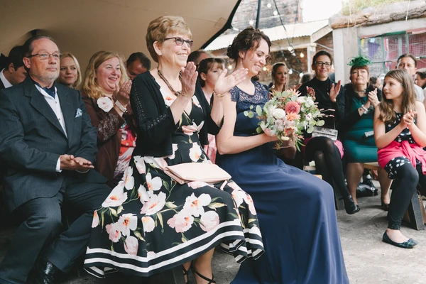 Wedding guests sitting and applauding at an outdoor ceremony — smiling older lady in floral dress