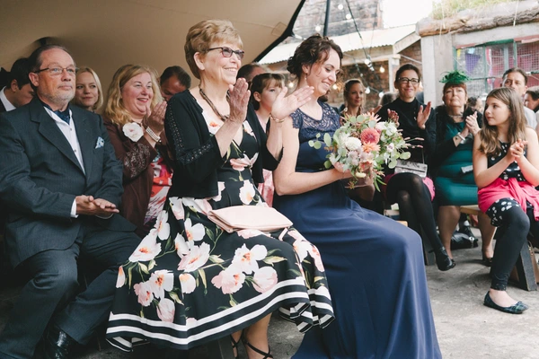 Wedding guests sitting and applauding at an outdoor ceremony — smiling older lady in floral dress