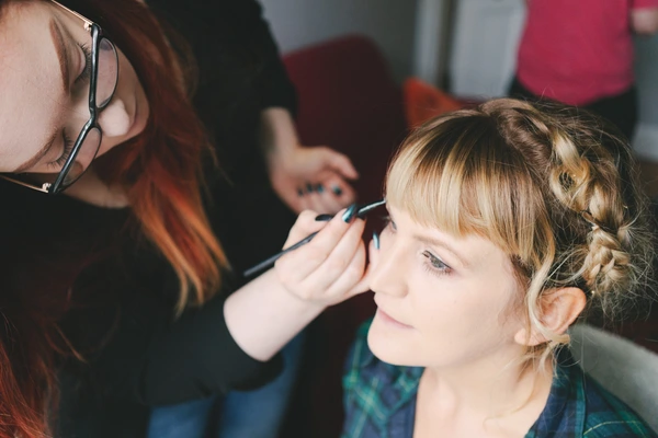 Young girl in profile, eyes closed, while a woman with glasses applies makeup carefully