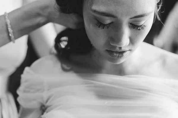 Bride with closed eyes, hand on silk dress, father smiling lovingly behind — black-and-white