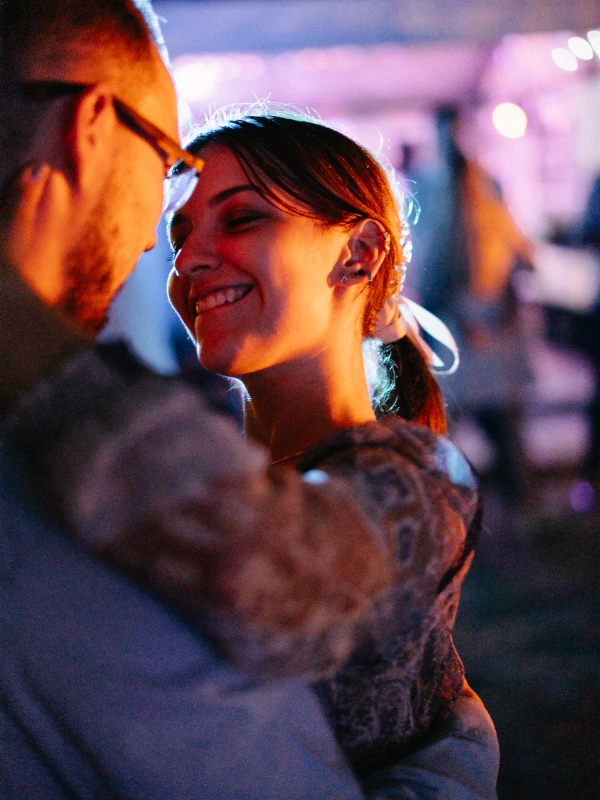 Young bride smiles radiantly at celebration — glowing evening lighting, emotional, happy moment, colorful ambient light.