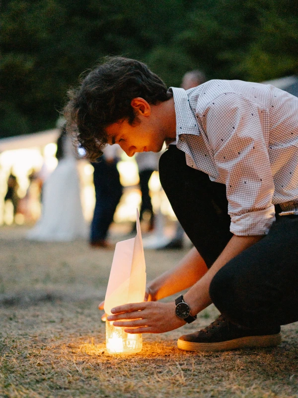 Guest lighting candle lantern at outdoor evening wedding reception with warm glow.