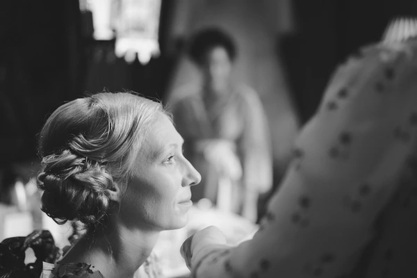 Woman in profile during the ceremony — gentle smile, elegant braided updo. Black-and-white.