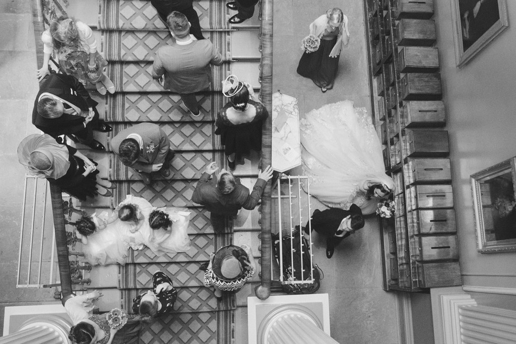Aerial view of the wedding — bride's white gown and groom's black suit visible, guests around