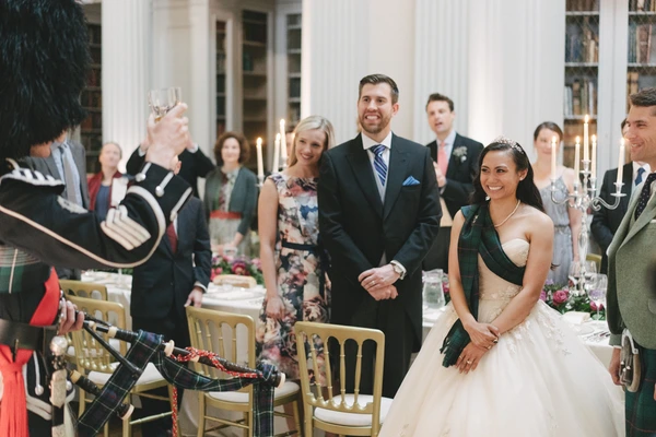 Bride and groom standing during the elegant dinner, guests congratulating — candlelit, white columns