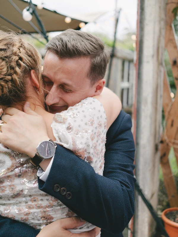Groom holds the bride in his arms — white sequined bridal dress, vintage garden with azaleas
