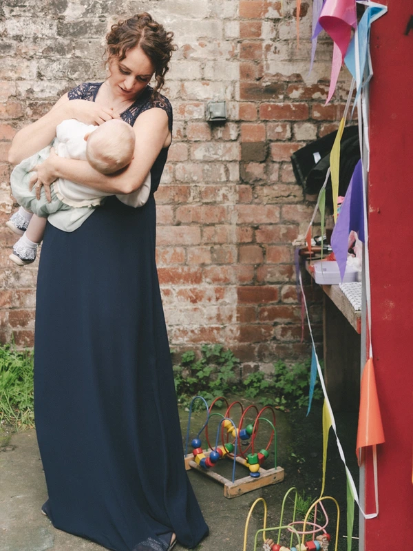 Mother lovingly holds her newborn in front of a rough brick wall, surrounded by toys