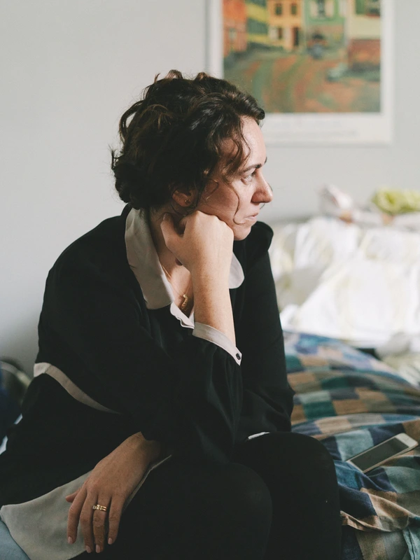 Woman in black suit sits on a bed, lost in thought — soft natural light, intimate moment