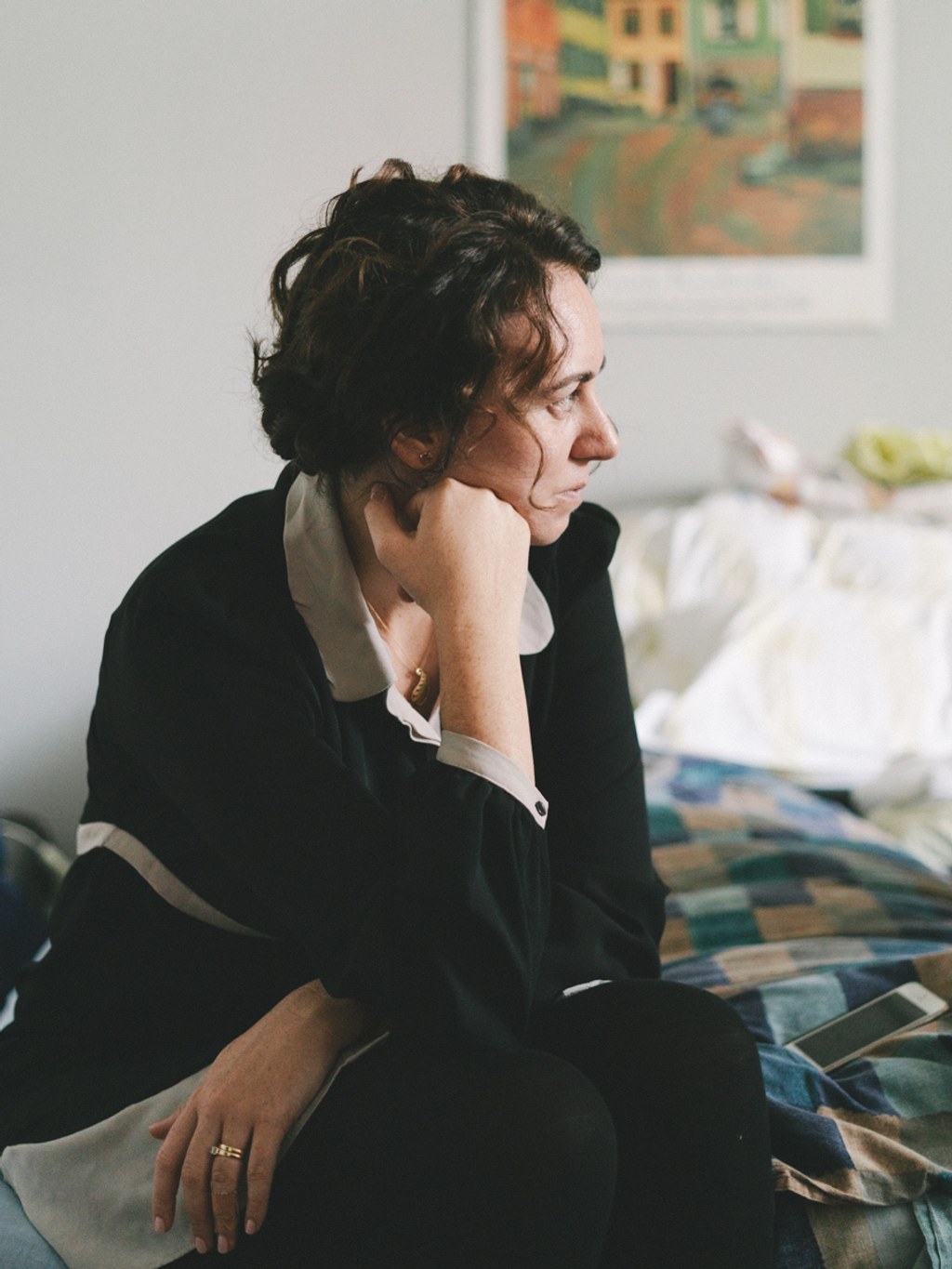 Woman in black suit sits on a bed, lost in thought — soft natural light, intimate moment