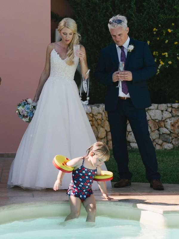 Bride and groom with champagne watch a little girl playing in the pool in a floral swimsuit