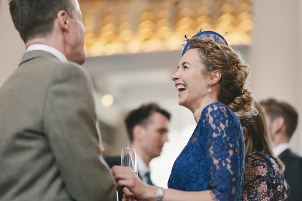 Woman in blue lace top smiling and talking with a man in grey suit, champagne in hand