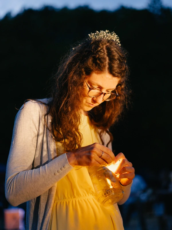 Woman in light dress holding lit lantern at dusk wedding with natural twilight background.