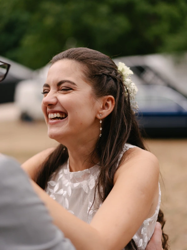 Bride's close-up smiling face with joy during wedding reception with groom nearby in natural light.