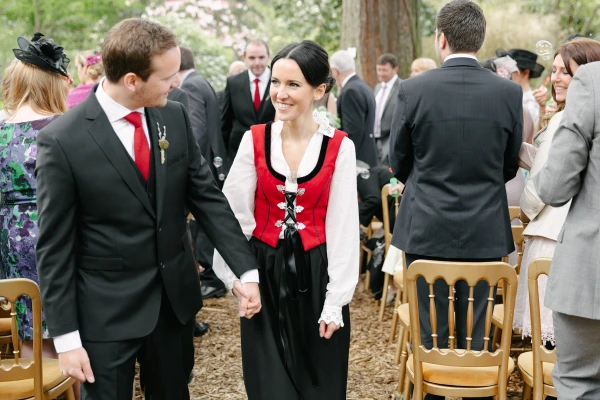 Bride and groom walking hand in hand smiling through the seated guests after the ceremony among the trees at the Royal Botanic Garden Edinburgh. Joyful recessional moment.