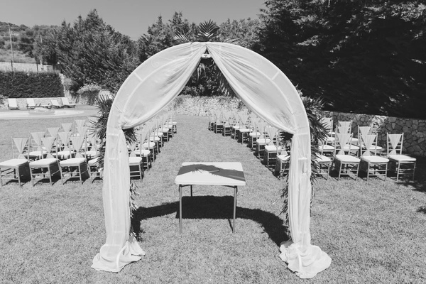 Outdoor ceremony venue in garden — white draped arch, rows of Chiavari chairs on green lawn