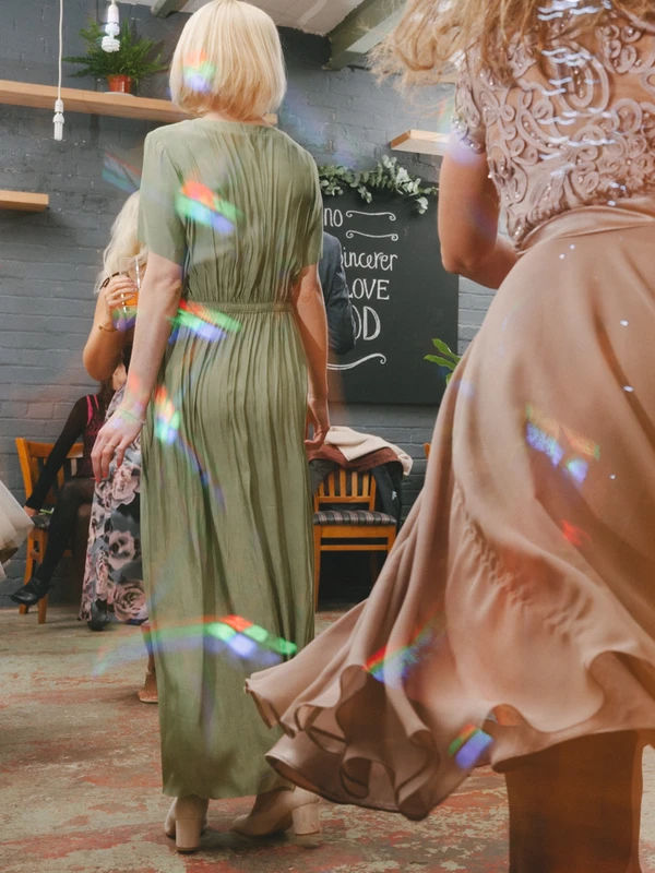 Female guests in long gowns at the loft-style venue — rainbow light beams on grey brick wall